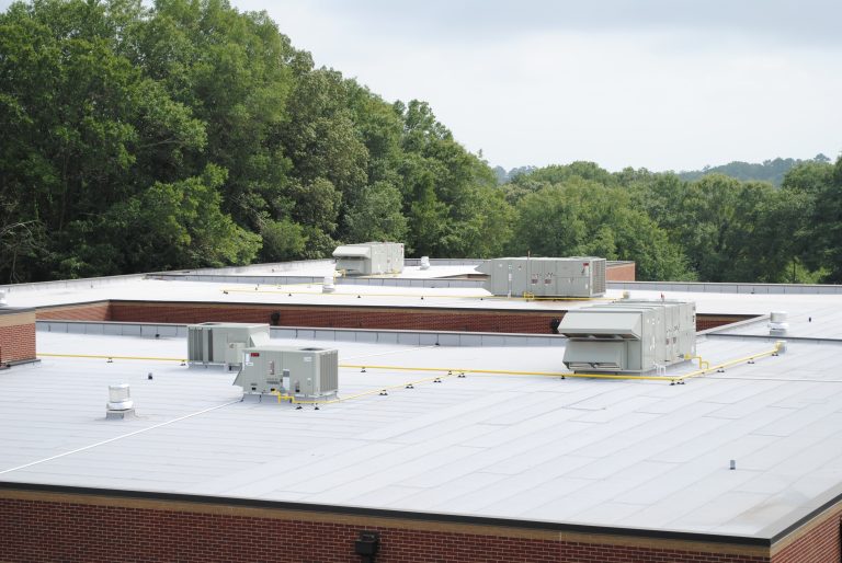 Commercial roofing system with HVAC units on a flat roof, surrounded by green trees, showcasing Grier Roofing's expertise in durable roofing solutions for industrial properties.