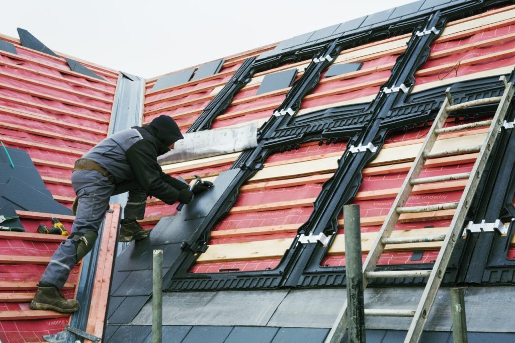 Roofer installing new tiles on a house roof, showcasing roofing repair work relevant to insurance claims and roof condition.