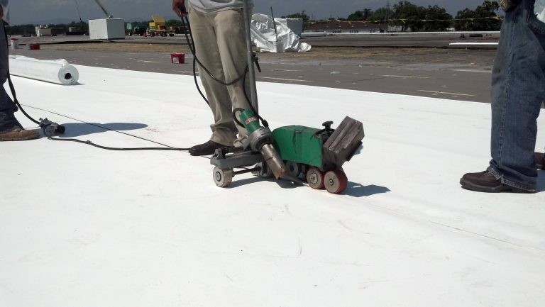 Workers using a roofing machine on a commercial white flat roof, demonstrating installation techniques for durable roofing solutions.
