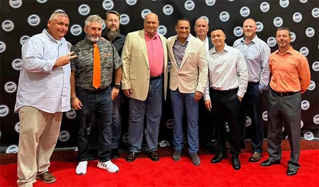 Group of men in business attire posing on a red carpet backdrop, representing Grier Roofing's team at an industry event, showcasing camaraderie and professionalism in the commercial roofing sector.