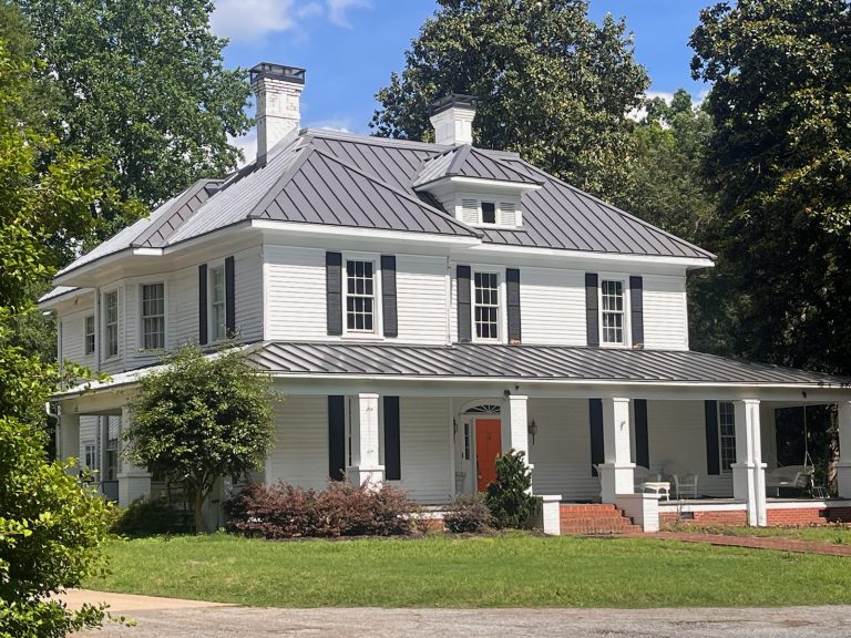Historic white house with a metal roof, surrounded by greenery, showcasing Grier Roofing's expertise in residential roofing solutions in Greenville, SC.