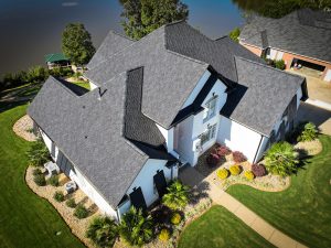 Aerial view of a residential home featuring a newly installed asphalt shingle roof, surrounded by landscaped gardens, showcasing Grier Roofing's commitment to quality and aesthetic appeal in roof replacements.