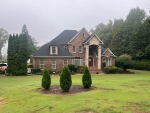 Residential home featuring a brick exterior and a stylish roof, surrounded by manicured landscaping, illustrating Grier Roofing's commitment to enhancing curb appeal and energy efficiency through quality roofing solutions.