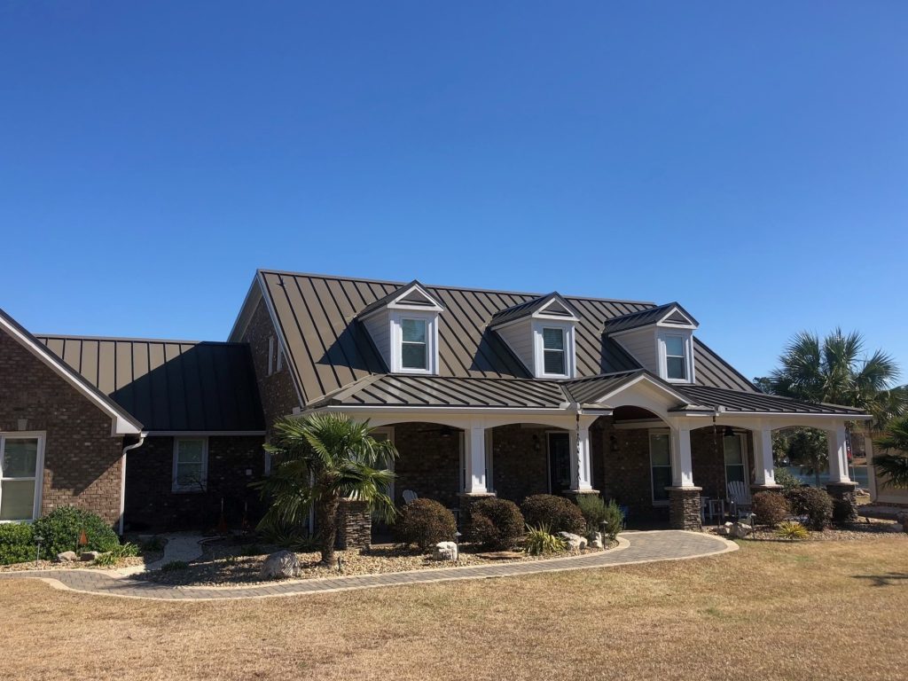 Modern home with a new metal roof, showcasing curb appeal and energy efficiency, surrounded by landscaping and clear blue sky, emphasizing the importance of roofing in home value.