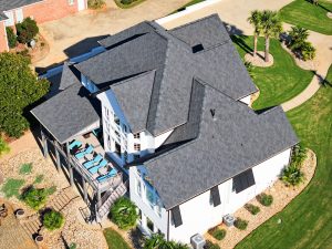 Aerial view of a residential home featuring a newly installed asphalt shingle roof, surrounded by landscaped gardens and outdoor seating, highlighting Grier Roofing's commitment to quality and aesthetic appeal in roof replacements.