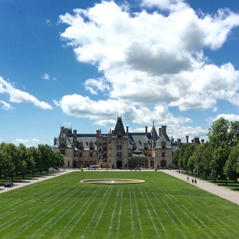 Biltmore Estate in Asheville, NC, featuring historic architecture, manicured lawns, and a vibrant blue sky, highlighting the city's cultural and artistic heritage.