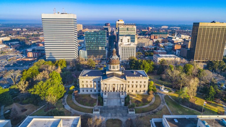 Aerial view of Columbia, South Carolina's skyline featuring the South Carolina State House and modern commercial buildings, highlighting the city's blend of government, education, and business infrastructure.