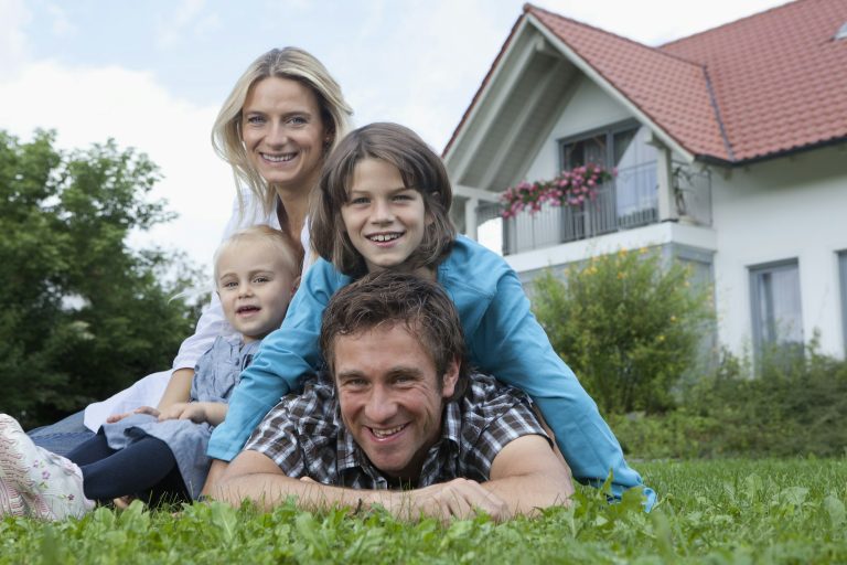 Family of four smiling together in front of a house, showcasing a welcoming home environment, reflecting Grier Roofing's commitment to family-oriented service in Atlanta, GA.