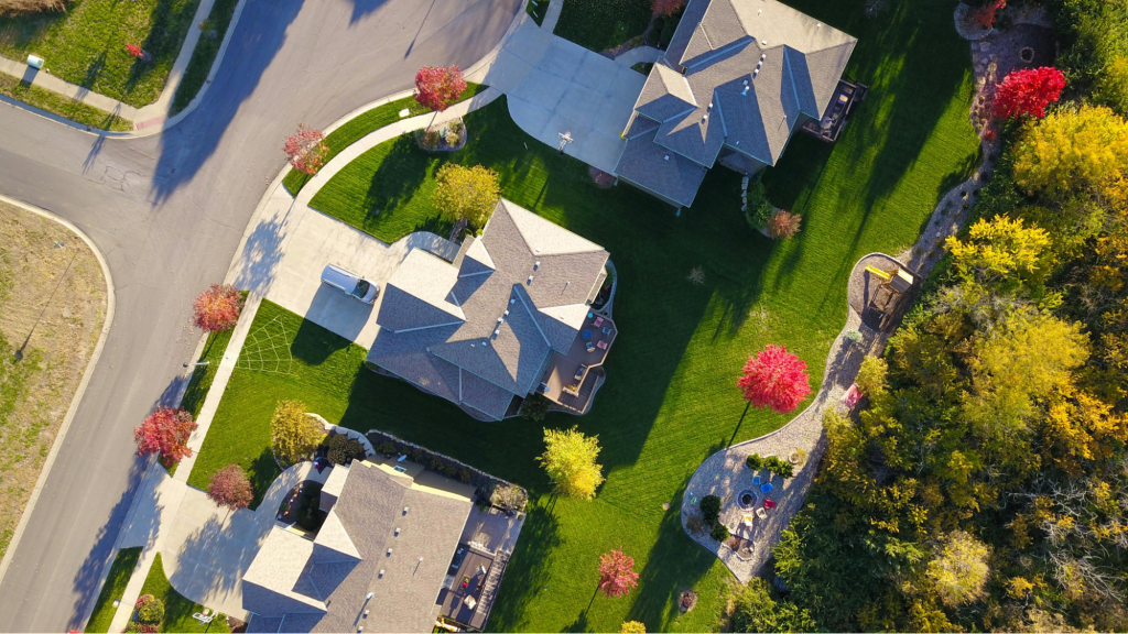 Aerial view of residential neighborhood showcasing well-maintained roofs, green lawns, and colorful autumn trees, emphasizing the importance of roof inspections and maintenance for homeowners.