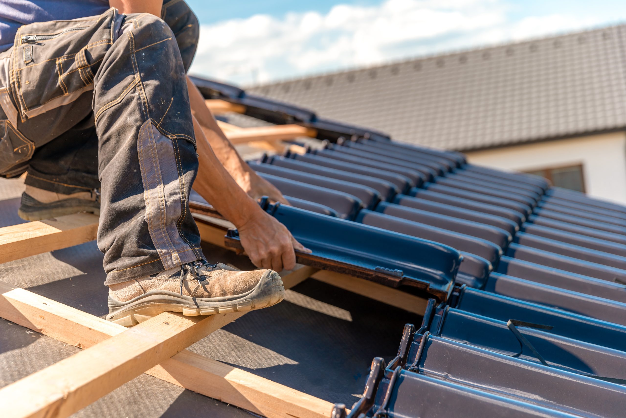 Roofer installing dark ceramic tiles on a residential roof, emphasizing quality craftsmanship and roofing services relevant to Grier Roofing's offerings.