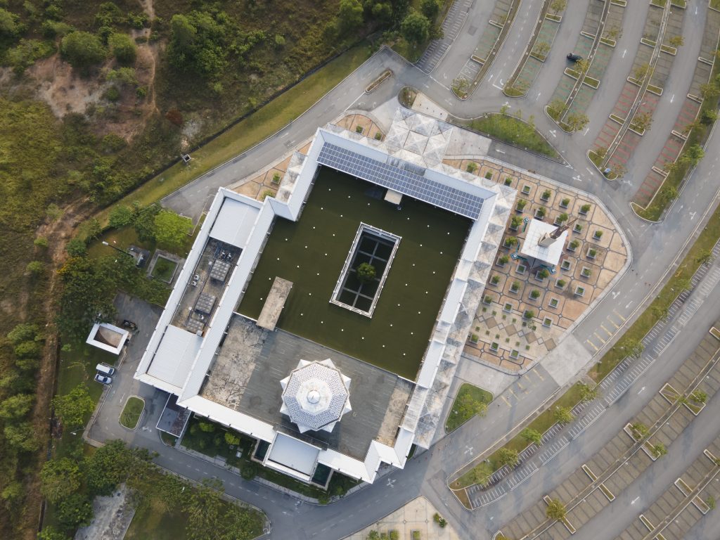 Aerial view of a modern commercial building with a flat roof, surrounded by landscaped areas and parking lots, illustrating features relevant to commercial flat roofing systems.