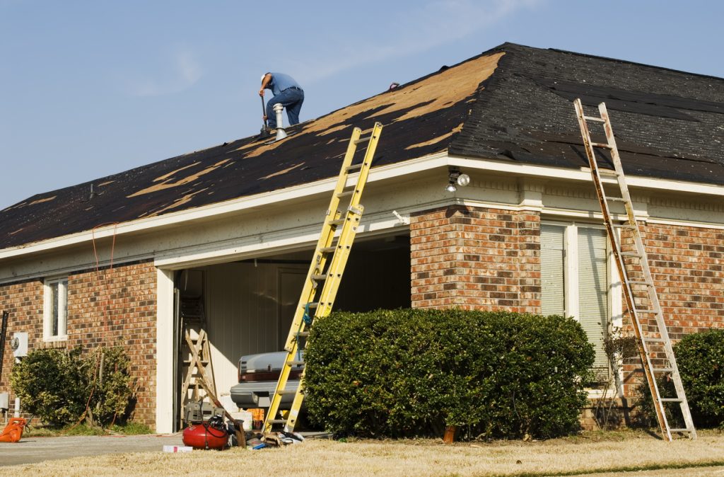 Roofing contractor replacing shingles on a residential roof, with ladders and tools visible, illustrating the roof replacement process relevant to home maintenance and improvement.