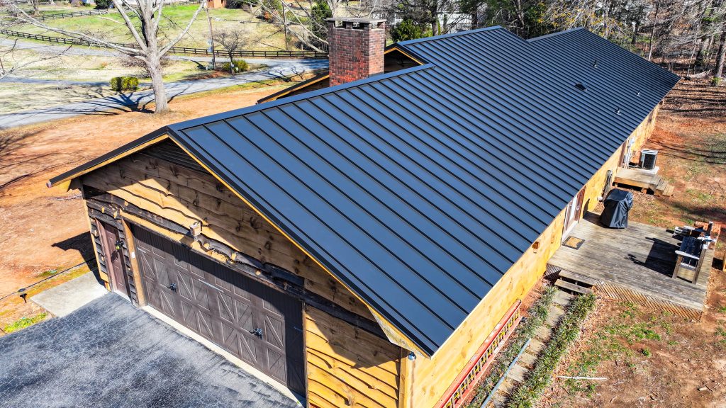 Aerial view of a residential building featuring a sleek black metal roof, showcasing Grier Roofing's quality installation and craftsmanship in a scenic outdoor setting.