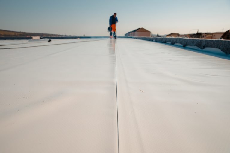 Worker walking on a newly installed white TPO roofing membrane, showcasing commercial roofing application for Atlanta businesses.