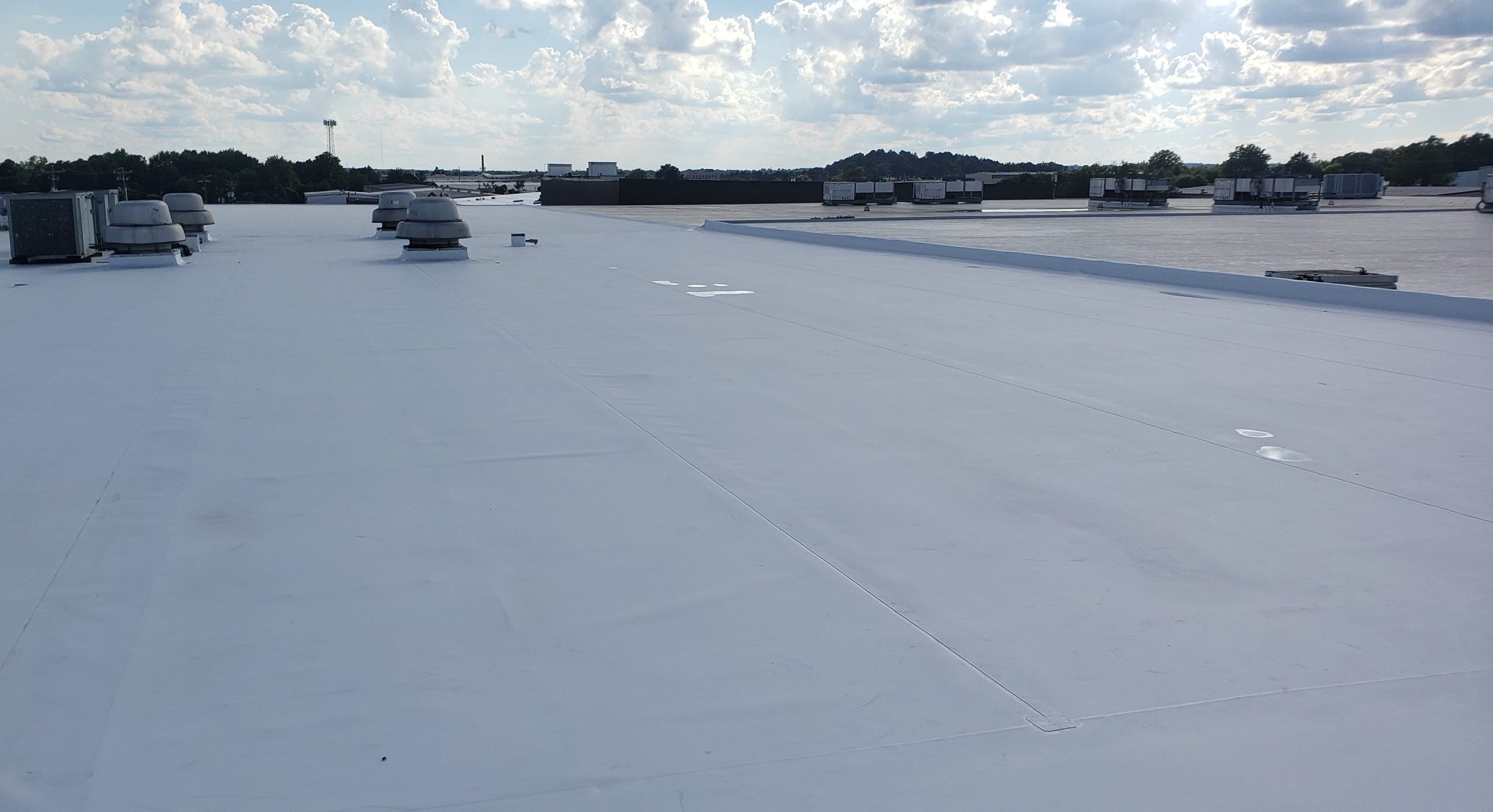 Flat commercial roof with white membrane, featuring ventilation units and a clear sky, emphasizing roofing maintenance and installation services.